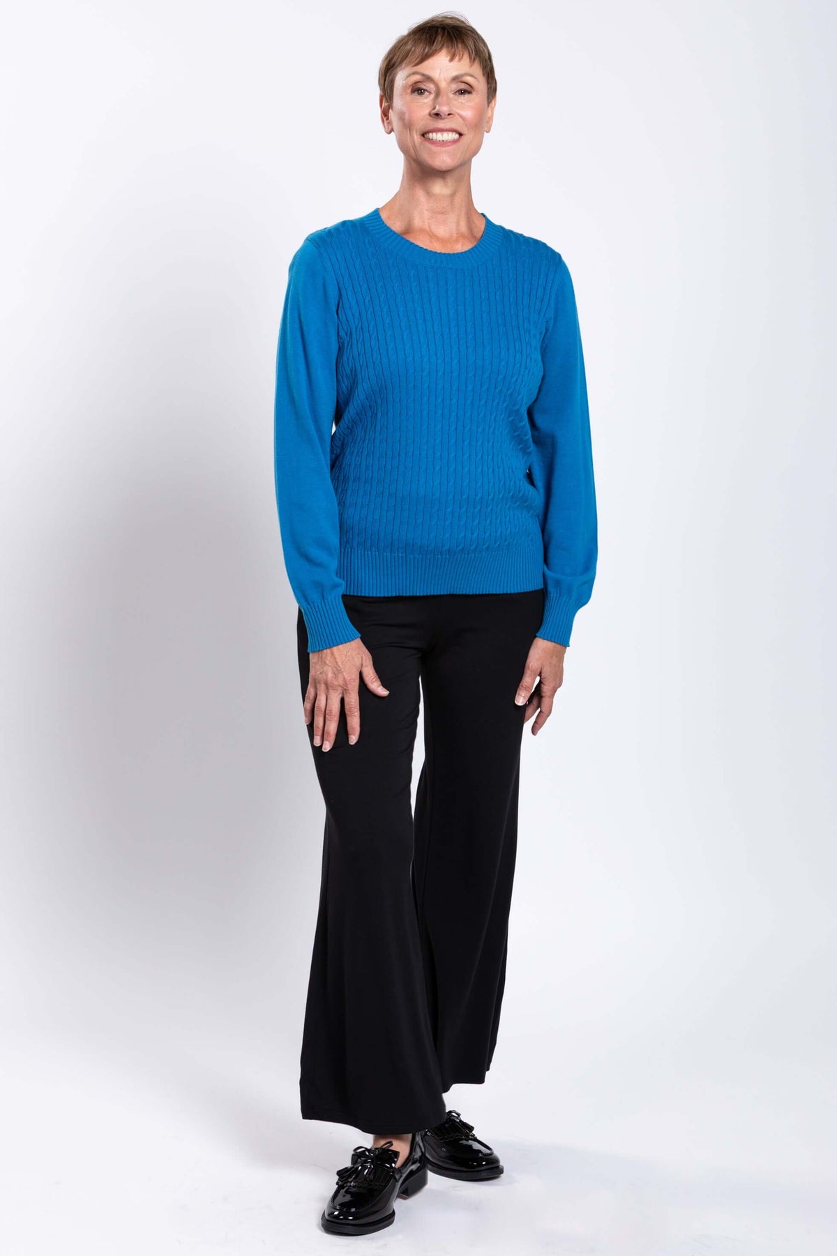 Smiling woman in blue cable knit sweater and black wide leg pants