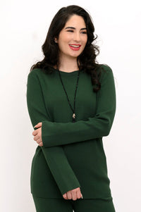 Smiling woman wearing an emerald green crew neck cotton sweater featuring a relaxed rectangular knit drape.