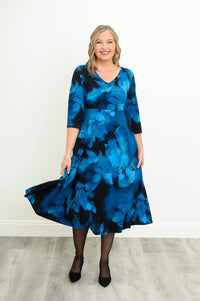Front view of a female model wearing a blue patterned bamboo cotton midi dress styled with simple black heels, against a white wall and gray floor