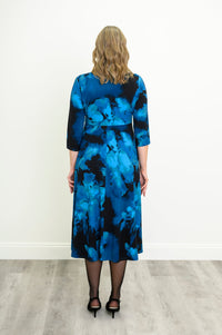 Back view of a female model wearing indigo patterned A-line midi dress highlighting the fluid skirt and full coverage, against a white wall and gray floor
