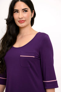 Close up front view of woman smiling wearing a scoop-neck dark purple sleep dress with a breast pocket