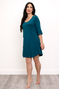 Full body view of woman smiling, wearing a teal scoop-neck sleep dress with black trim