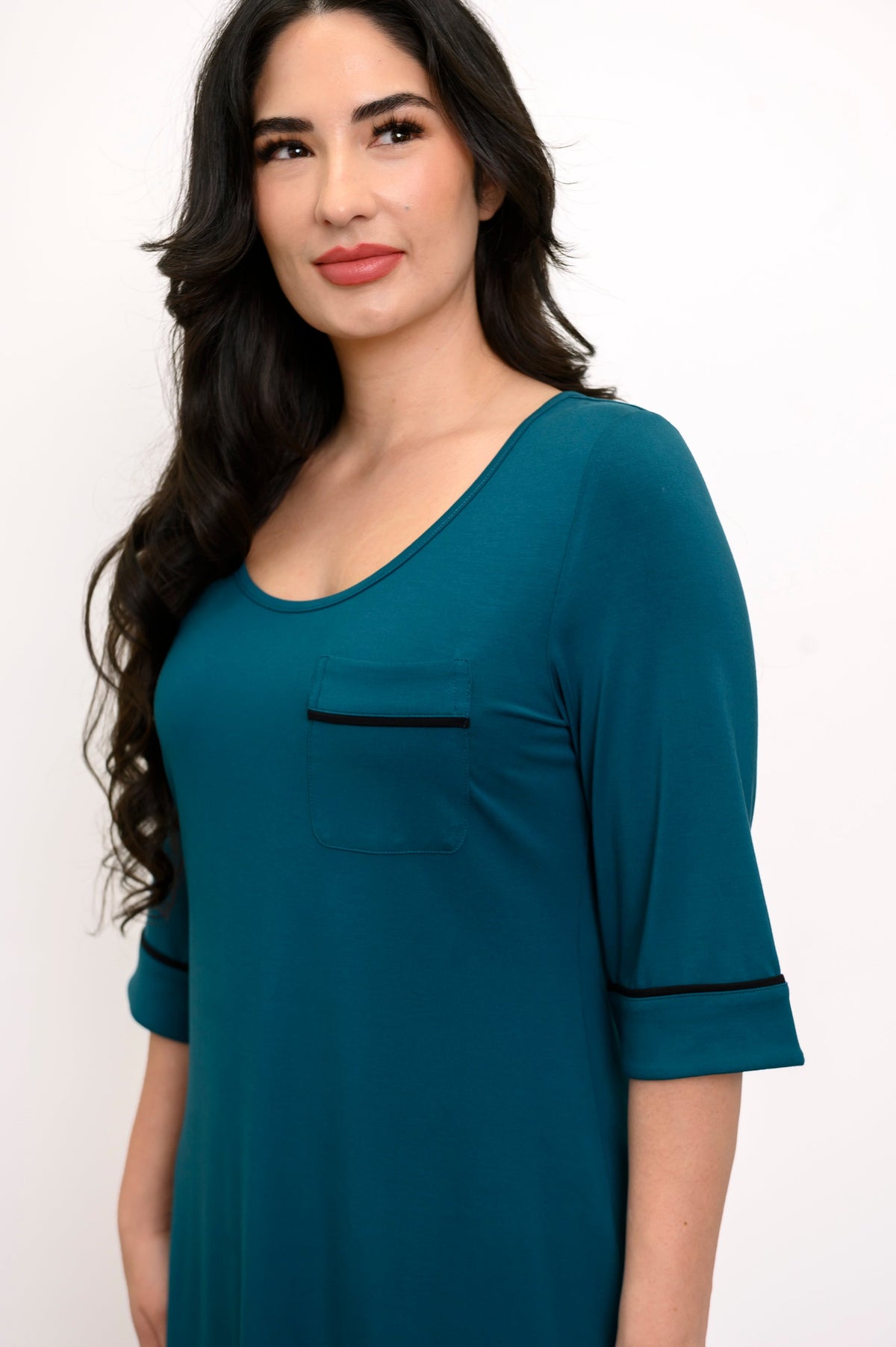 Close up view of woman smiling and looking off center as she wears a half-sleeve teal colored sleep dress