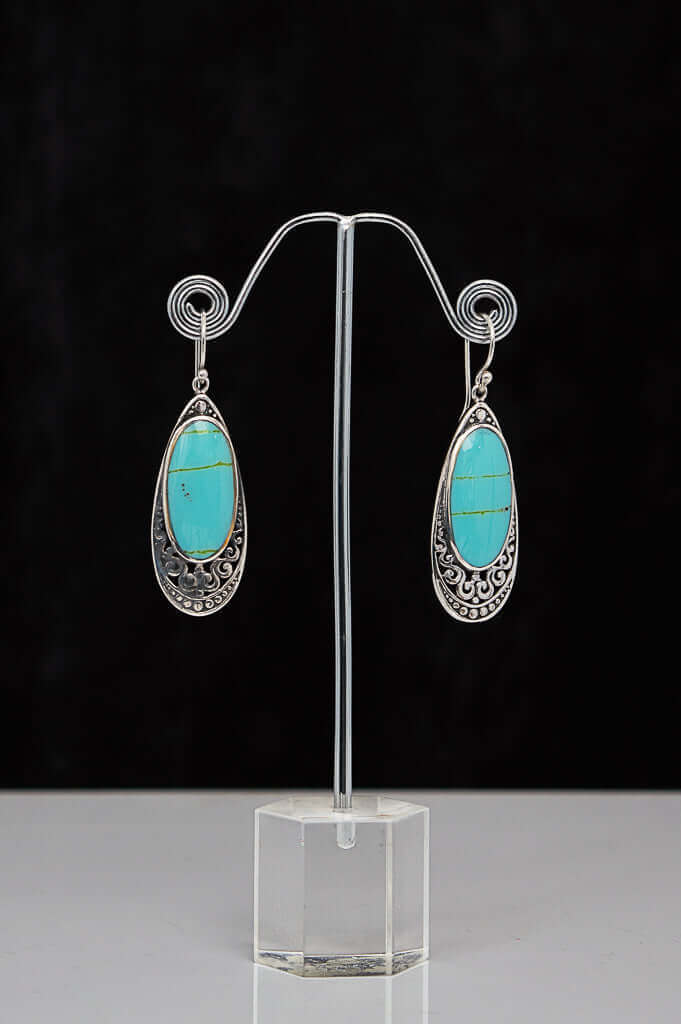 Pair of 925 sterling silver earrings with turquoise teardrop stones on display stand