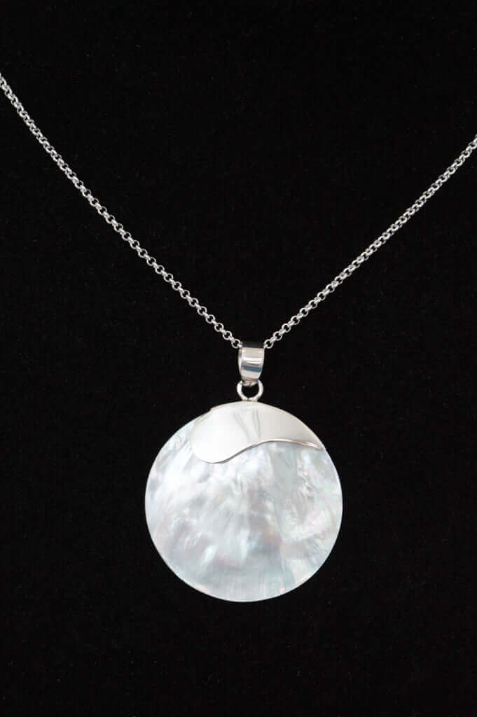 Close-up of a sterling silver necklace with a round polished shell pendant on black background