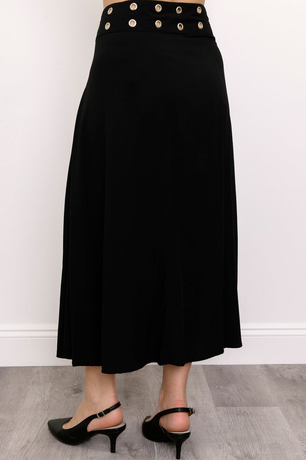 Woman wearing long black skirt with grommet details and black shoes on a white background, back view