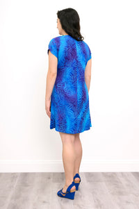 Woman wearing a blue patterned dress and blue sandals on a white background, back view