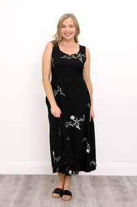 Woman wearing a long black sleeveless dress with white seashells and sandals against a white background, front view