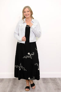 Woman wearing a long black dress with white seashells, a white jacket against a white background, front view