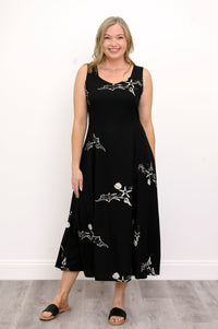 Woman wearing a long black sleeveless dress with white seashells and sandals against a white background, front view
