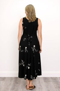 Woman wearing a long black sleeveless dress with white seashells and sandals against a white background, back view