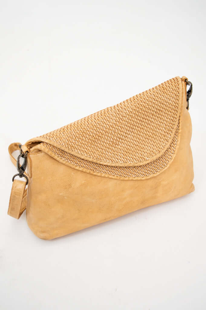 Tan leather crossbody bag with woven flap on white background
