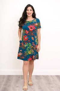 Front view of woman posing with her hand in the pocket of her floral print dress against a white background