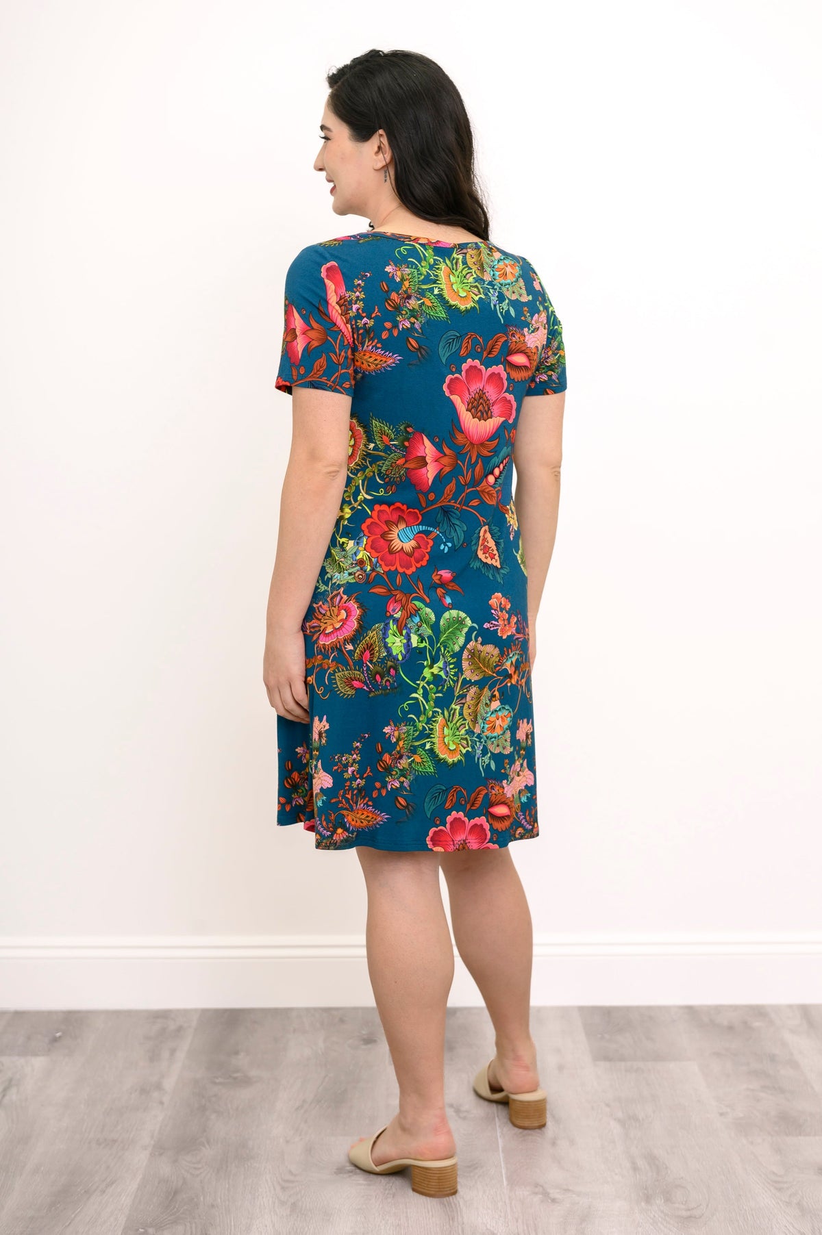 Woman with her back turned to the camera wearing a multicolor floral dress and beige sandals