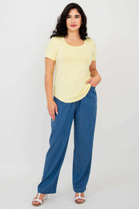 Full body view of woman wearing Tessa Tee in butter yellow with blue pants, hand in pocket