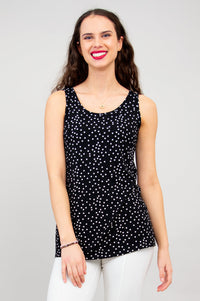 Woman wearing a black and white polka dot sleeveless top with a round neckline, relaxed fit, and hip-length silhouette, styled with white pants