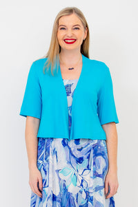 A woman wearing a turquoise colored jacket with short sleeves, paired with a printed dress.