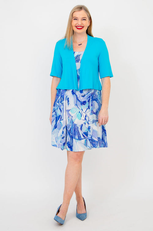 Woman smiling in half-sleeve flared turquoise shrug and blue floral dress