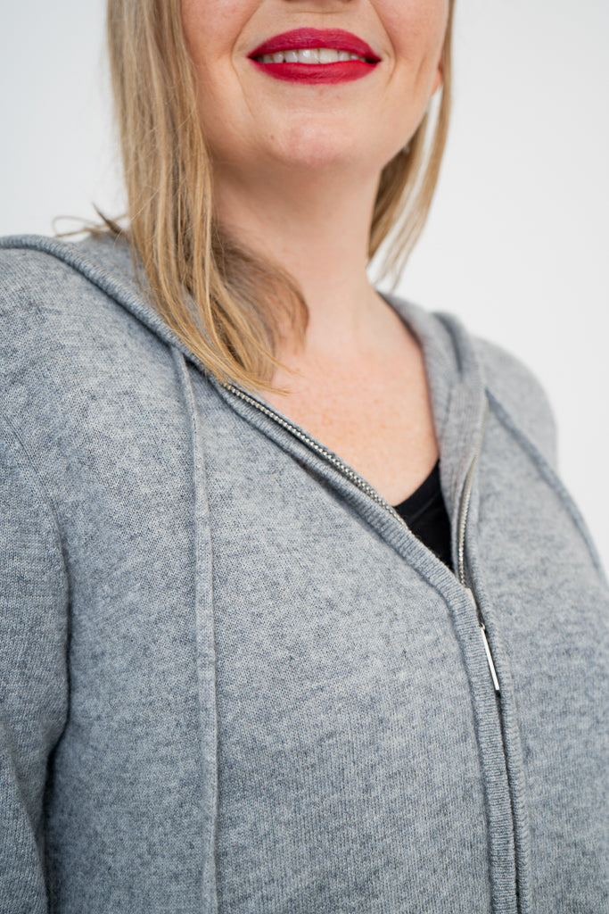 Close-up shot of woman wearing a grey zip-up sweater on a black top and wearing red lipstick