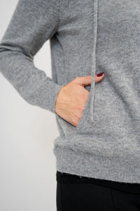 Close-up picture of woman putting her hand in the pocket of a grey sweater against a white background
