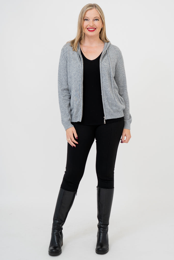Front view of woman wearing a grey sweater, black pants, and black boots against a white background