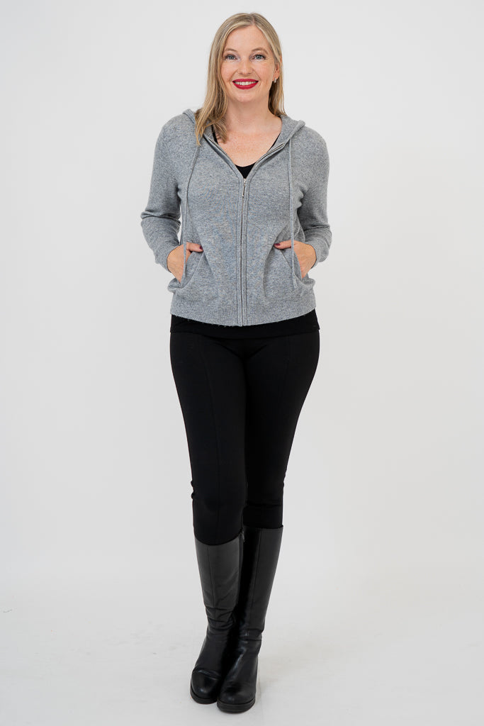Front view of woman wearing a grey sweater, black pants, and black boots against a white background