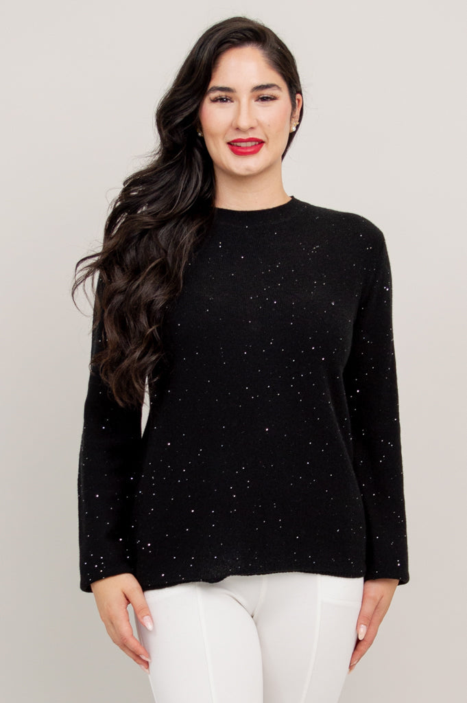Full length view of a woman wearing a black sparkly long sleeve sweater styled with white pants.