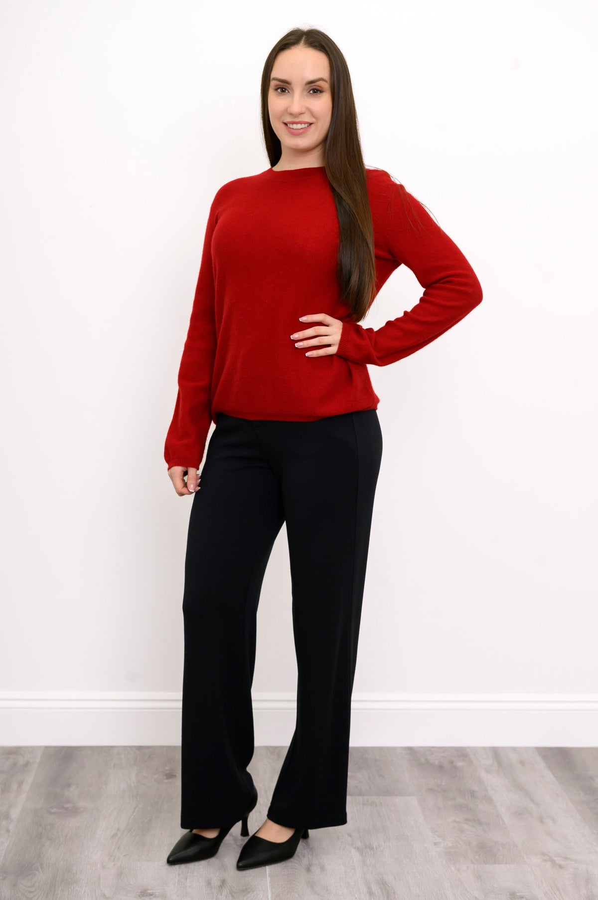 Woman smiling in red knit sweater, relaxed fit black pants, and black pumps