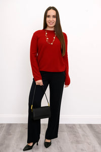 Woman wearing outfit featuring true red jumper, black pants, pearl neckalce, and black purse