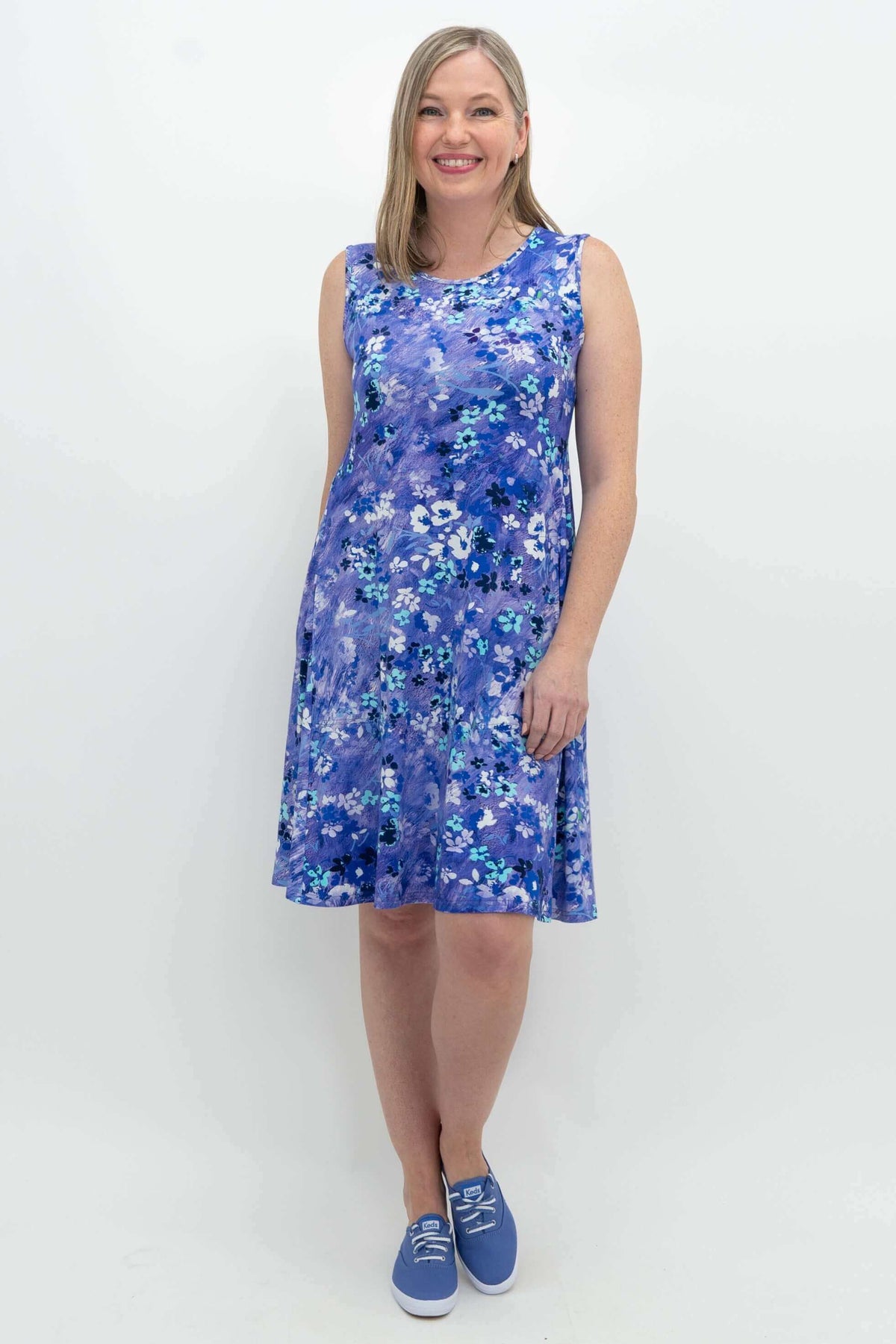 Front view of woman wearing a sleeveless blue floral dress with sneakers