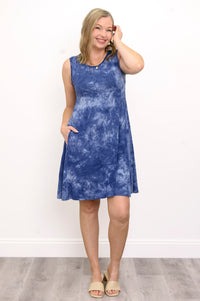 full body view of woman with her hand in her hair modelling a blue tie-dye print dress and cream sandals