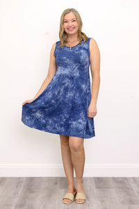 Front view woman playing with the hem of her blue tie-dye dress and smiling