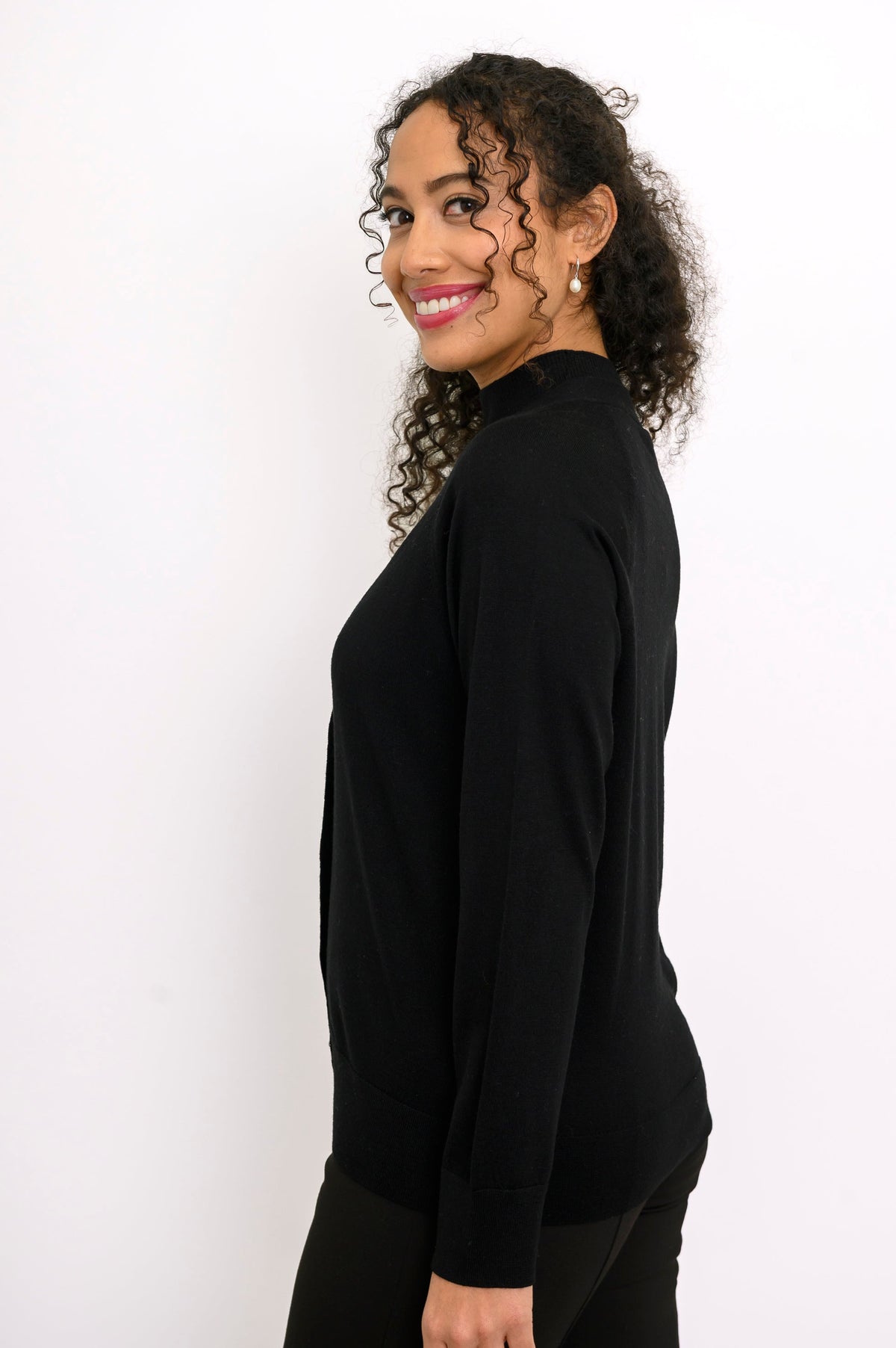 Side profile view of a woman wearing a long sleeve black merino wool v-neck cardigan sweater.