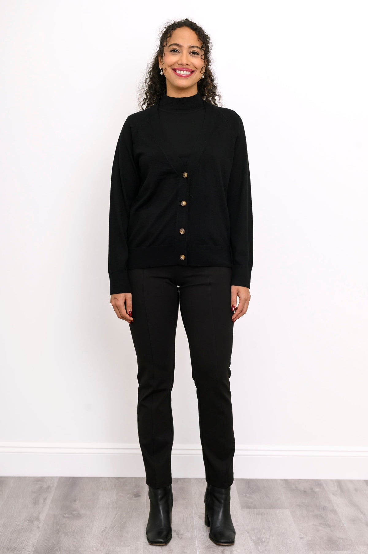 Full length view of a woman wearing a black merino wool v-neck cardigan sweater and black pants.