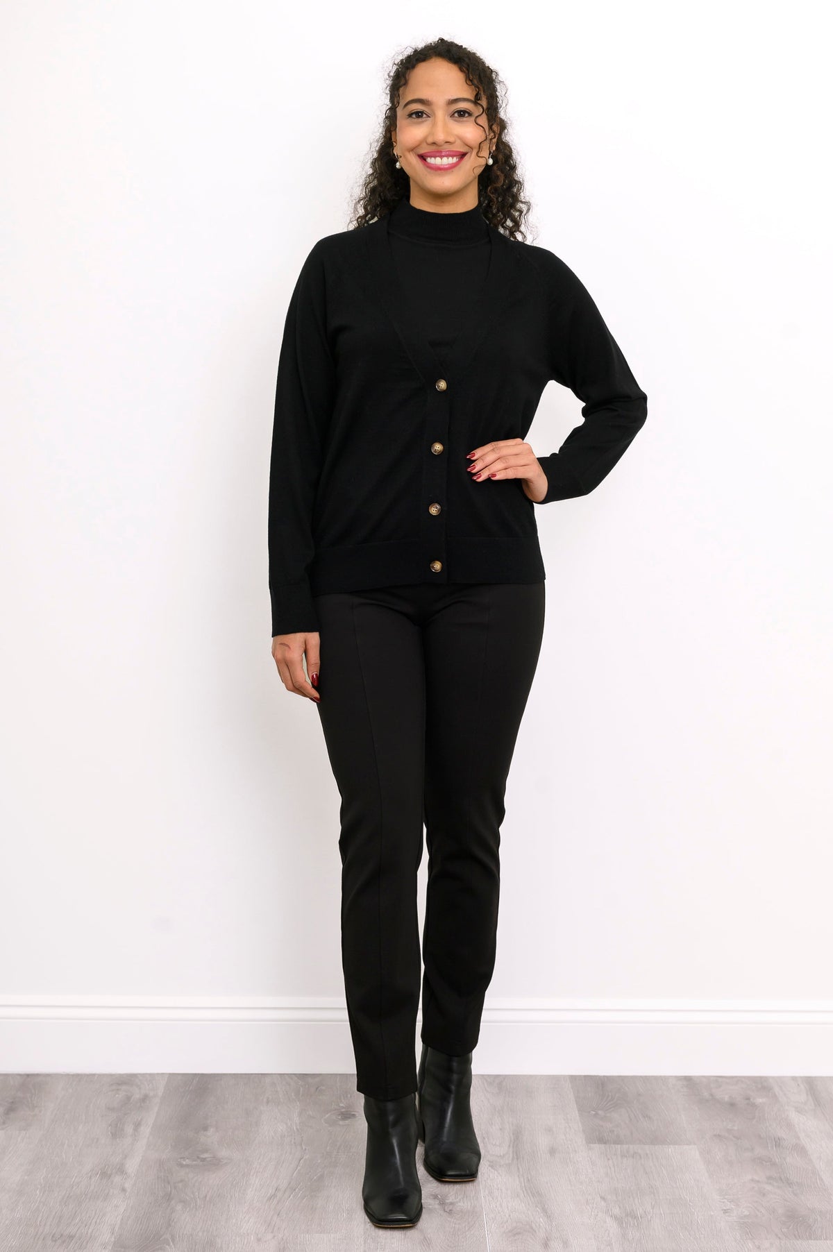 Front view of a woman wearing a black merino wool button down cardigan layered over black pants.