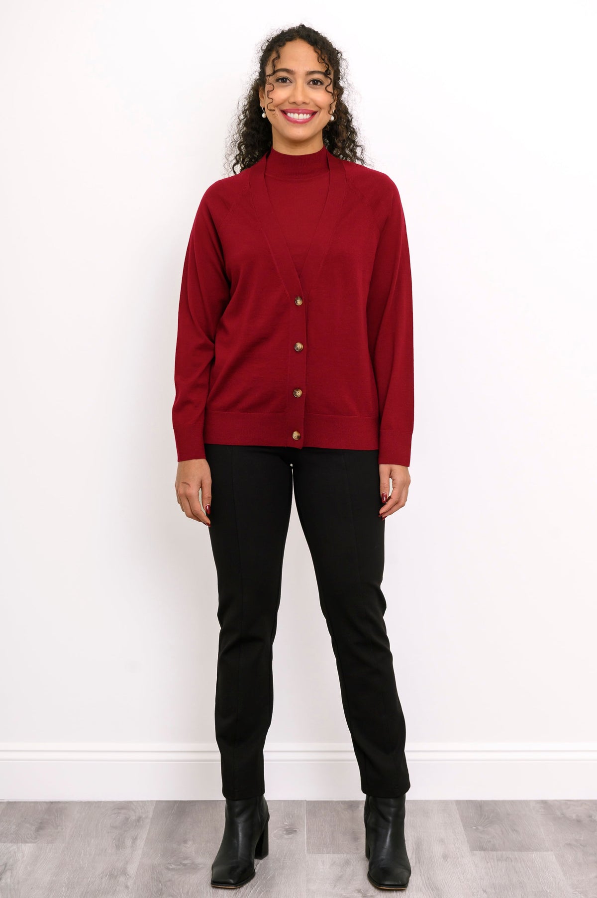Front view of a woman wearing a dark red merino wool button down cardigan layered over black pants.