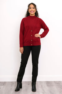 Woman modeling a hip length deep red fine wool cardigan with marled buttons and black trousers.