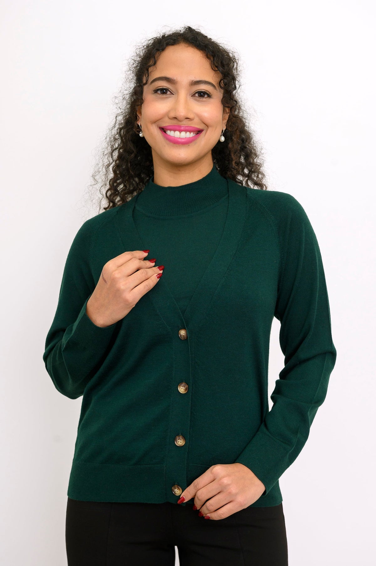 Studio portrait of a woman modeling a dark green fine wool button up cardigan over a sleeveless top.