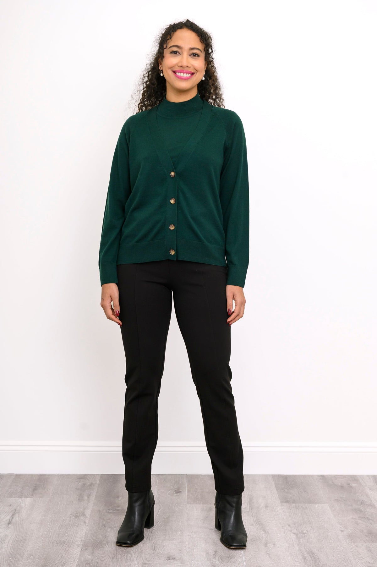 Full length shot of a woman in a deep green fine knit wool cardigan sweater styled with black boots.