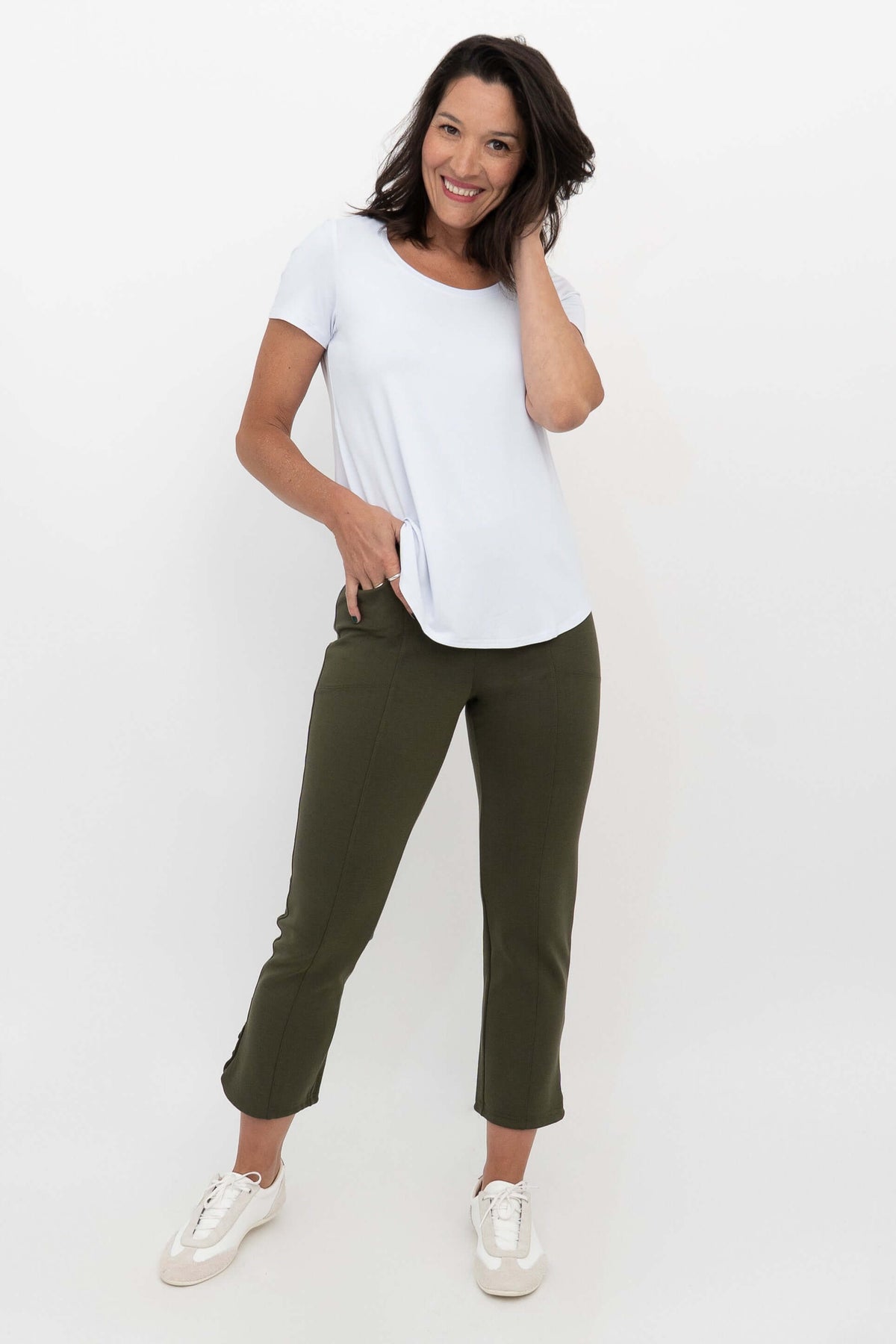 Woman in olive green crop pants and white t-shirt, hand in pocket, angled view