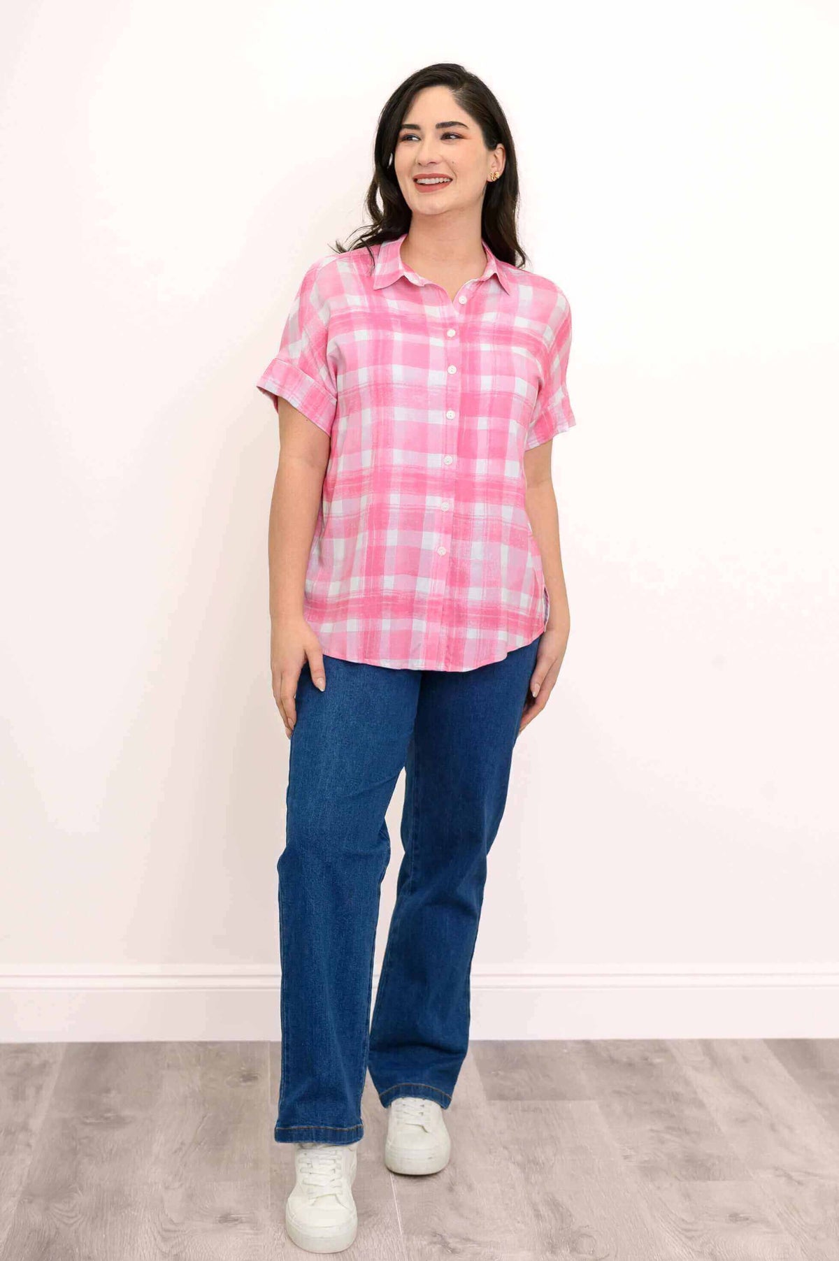 Side-facing woman in pink plaid short sleeve blouse with jeans and white sneakers