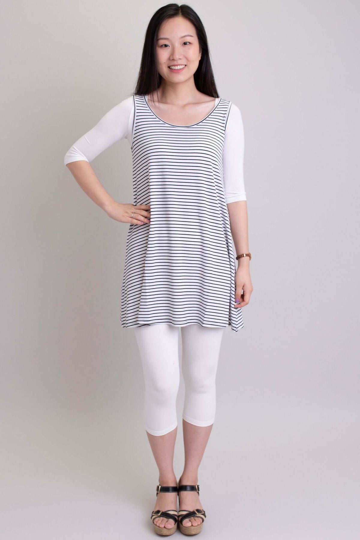 Woman in white Instant Sleeve bamboo bolero, striped tunic, and white capris posing with hand on hip