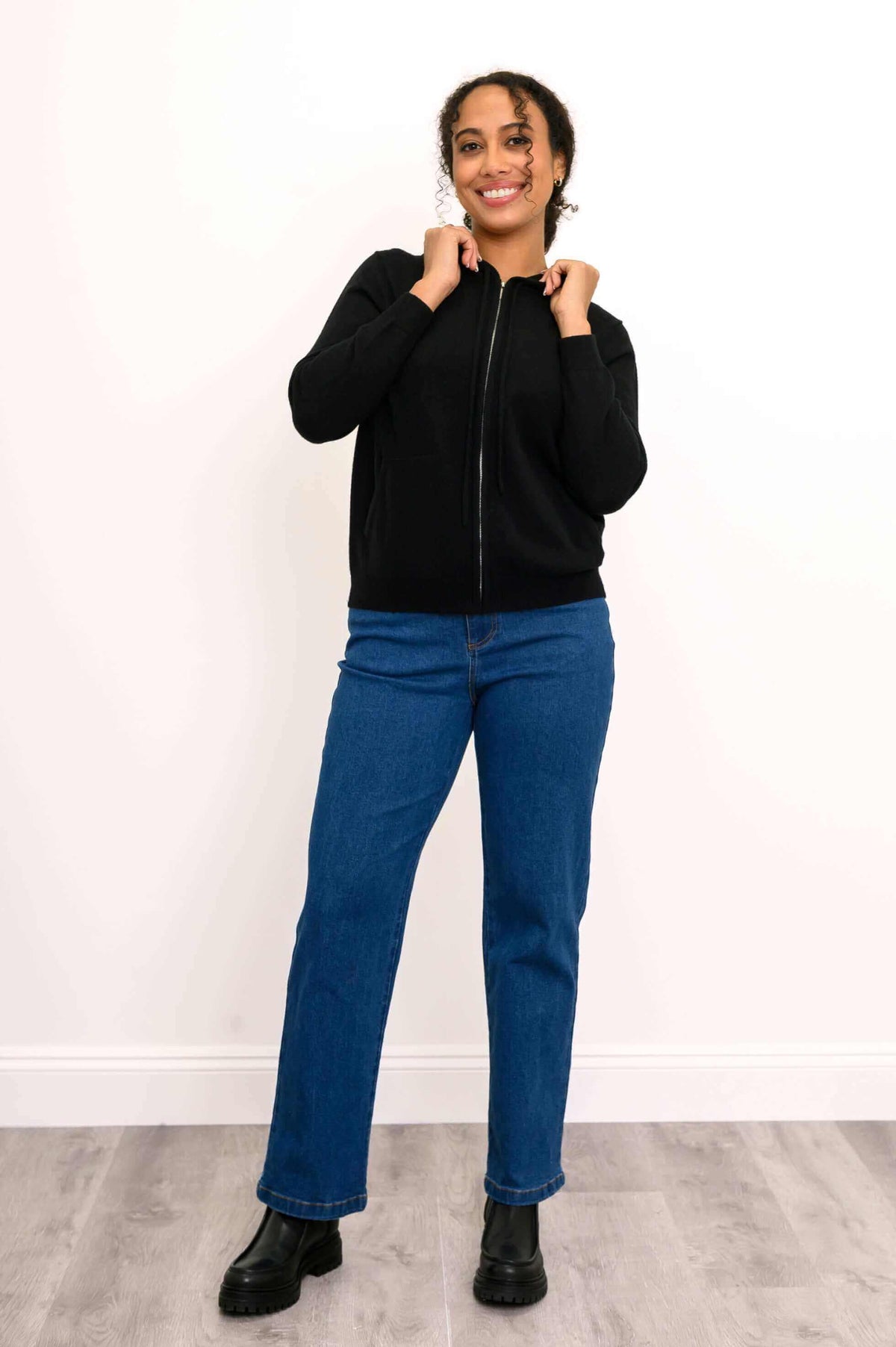 Full body view of a woman in a black wool-cashmere hoodie and blue jeans