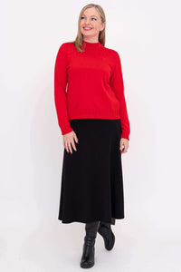 Woman standing in a red sweater and black skirt with black boots