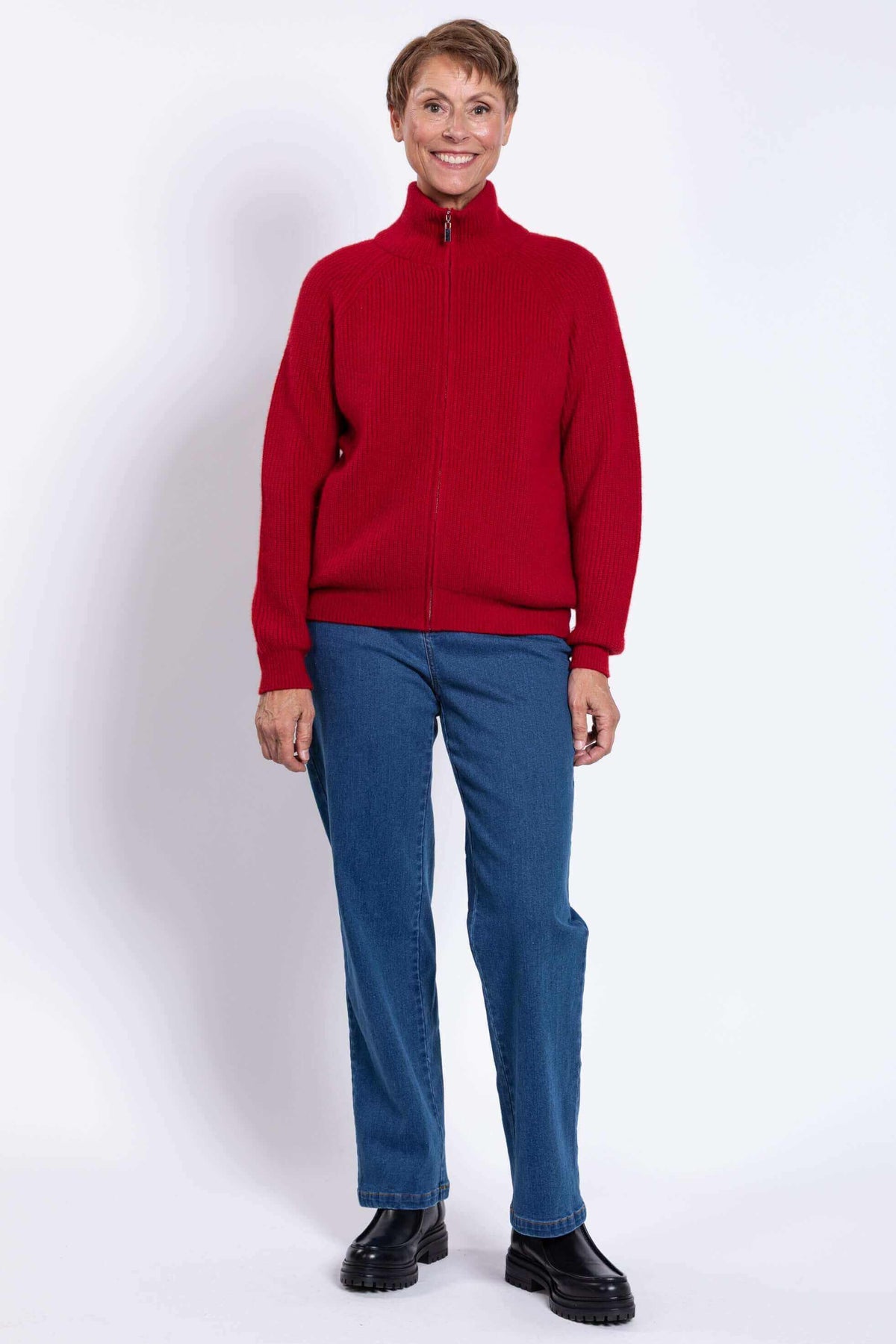 Smiling woman in a red wool-cashmere cardigan, standing with hands at sides