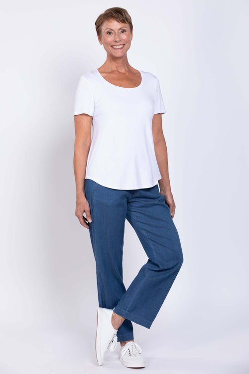 Woman wearing blue tencel denim pants and white t-shirt, standing and smiling