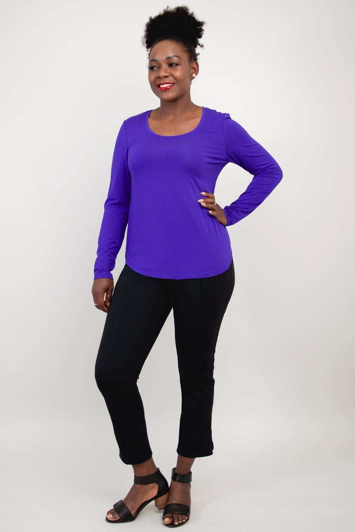 Woman standing in purple long sleeve scoop neck shirt and black pants