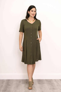 Woman with necklace wearing olive button-front dress, hands in pockets