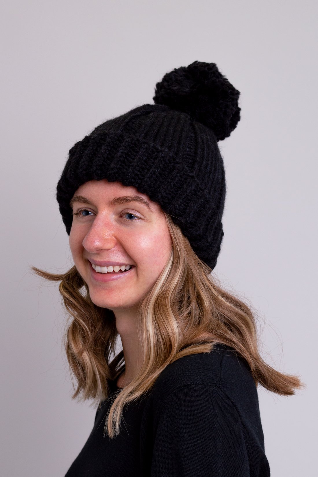 Women's black knit toque wool hat with pompom.